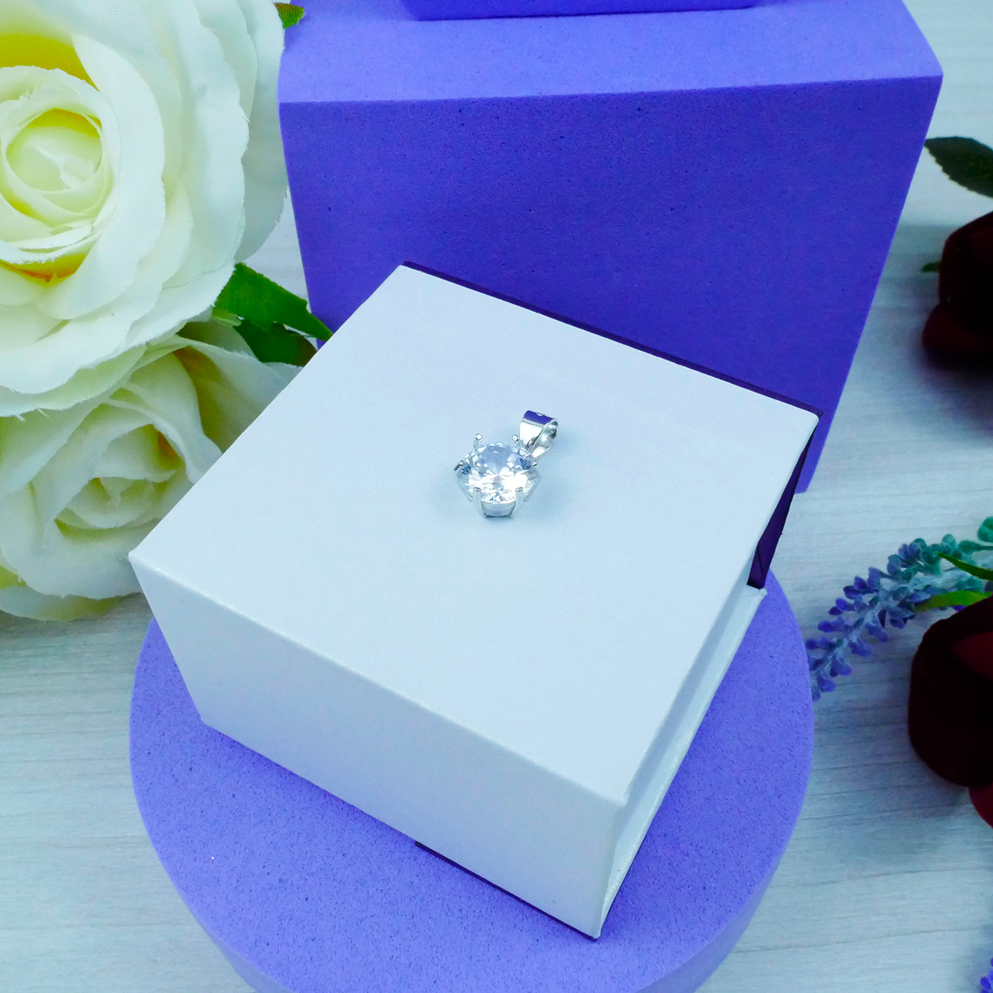 Silver earring in a white box with purple base and white roses in the background