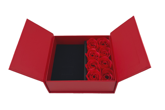A red jewellery box with eight rose petals inside, accompanied by a matching red presentation bag with a rope handle.