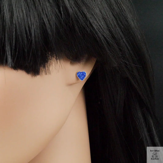 Blue heart-shaped earring worn by a person with black hair on a dark background