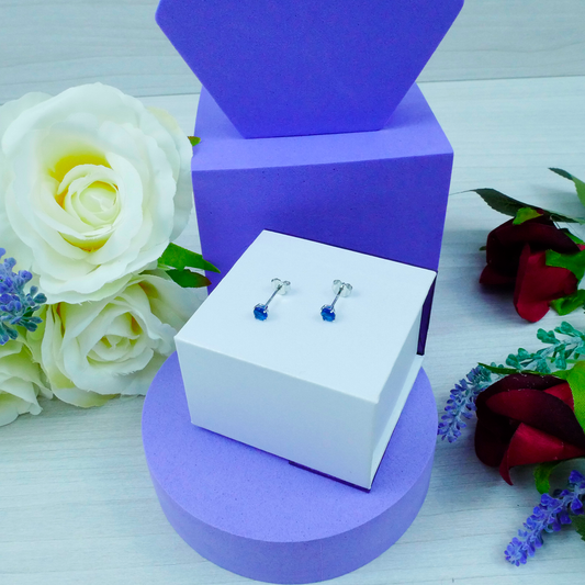 Pair of blue earrings on a white box with purple and white roses in the background