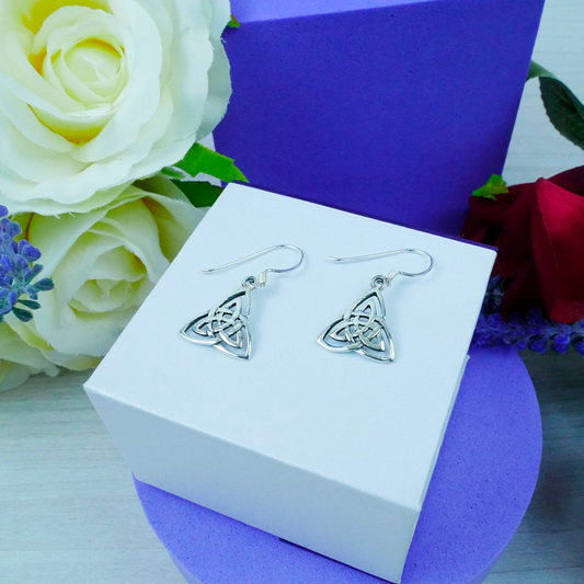 Silver Celtic knot earrings on a white box with flowers in the background