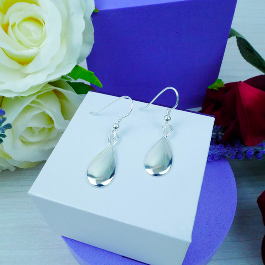 Silver teardrop earrings on a white stand with flowers in the background