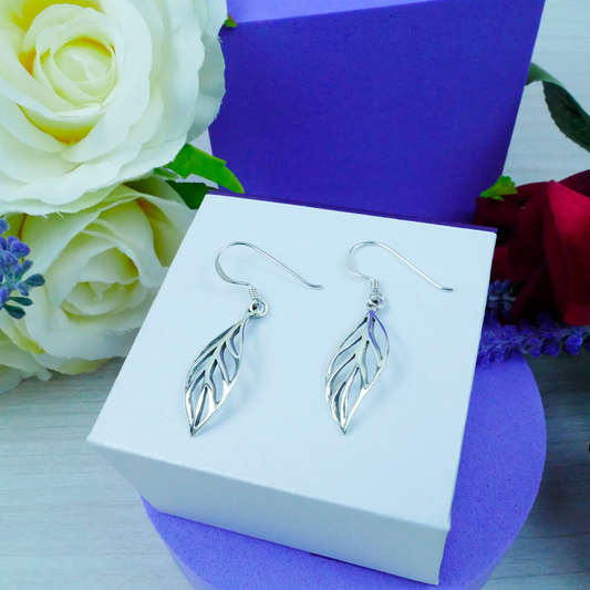 Silver feather-shaped earrings on a white box with flowers in the background