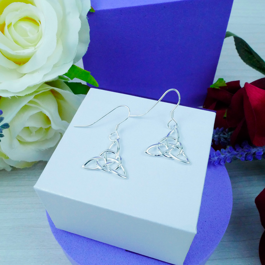 Silver Celtic knot earrings on a white box with flowers in the background