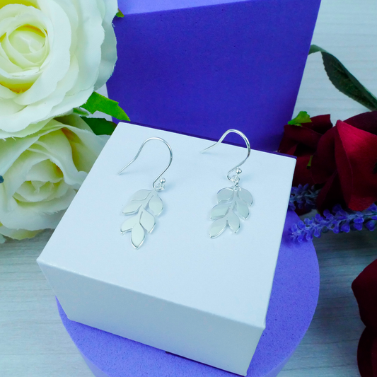 Silver leaf earrings on a white box with flowers in the background