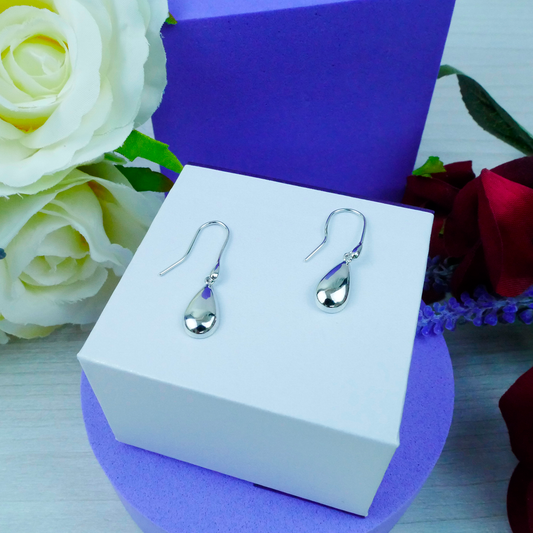 Silver teardrop earrings on a white box with flowers in the background