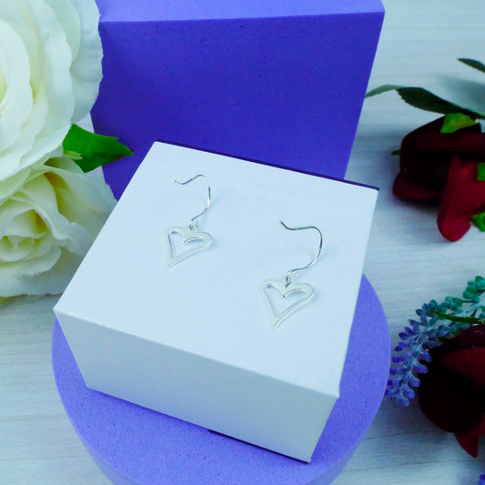Heart-shaped earrings on a white box with a purple background and flowers.