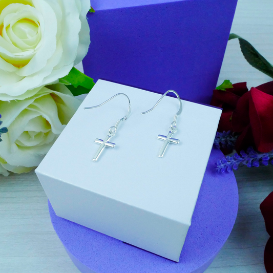 Silver cross earrings on a white box with flowers in the background