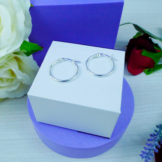 Silver hoop earrings on a white box with flowers in the background