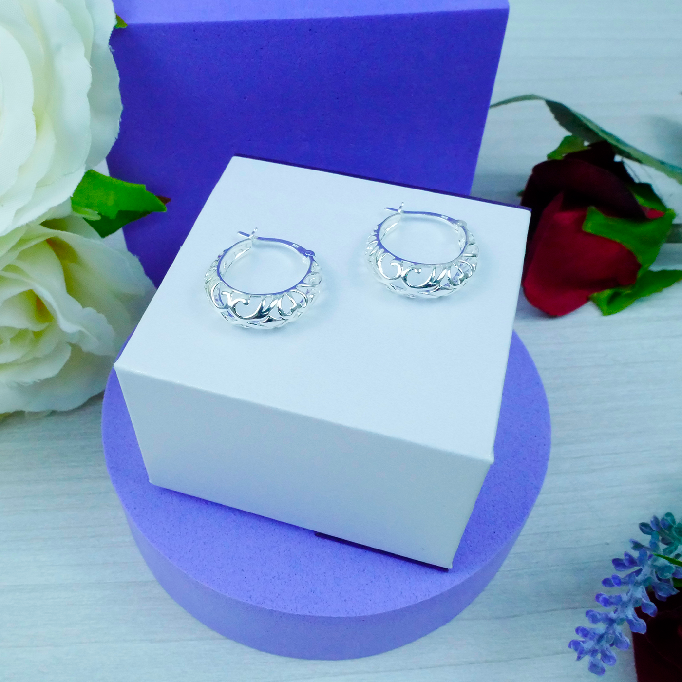 Silver hoop earrings on a white box with purple base and floral decorations.