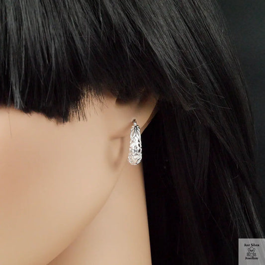 Close-up of a person wearing a silver hoop earring with a dark background
