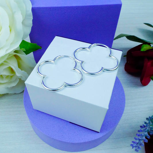 Silver four-leaf clover earrings on a white box with a purple background and flowers.