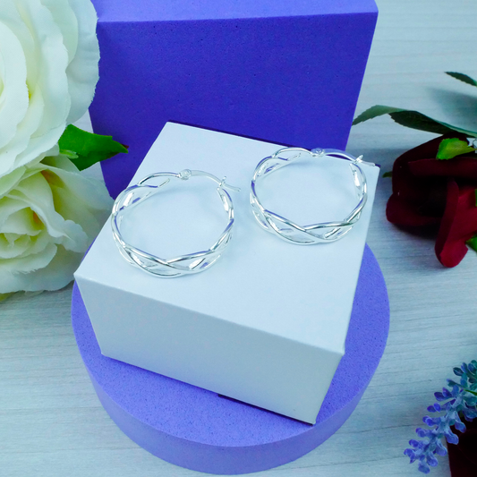Silver hoop earrings on a white box with purple base, surrounded by flowers.