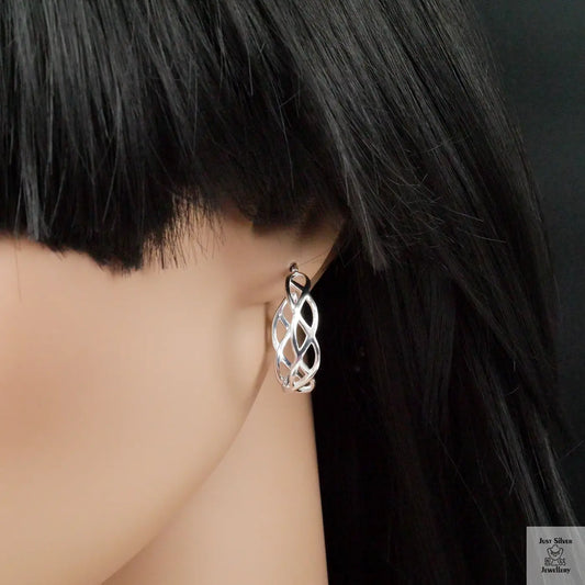 Silver earrings worn by a person with black hair against a dark background