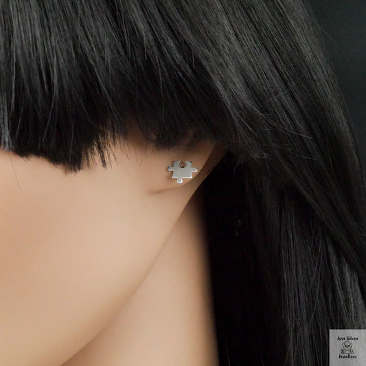 Silver puzzle piece earring worn by a person with black hair.