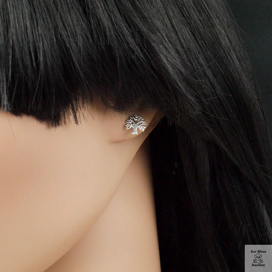 Silver tree-shaped earring on a mannequin ear with black hair.