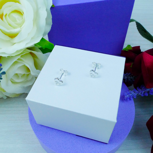Silver earrings in a white box with purple interior, surrounded by flowers.