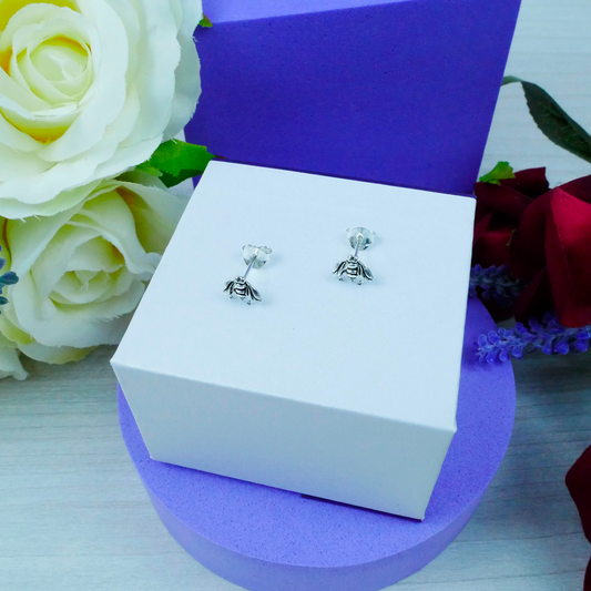 Silver bee earrings in a white box with flowers in the background