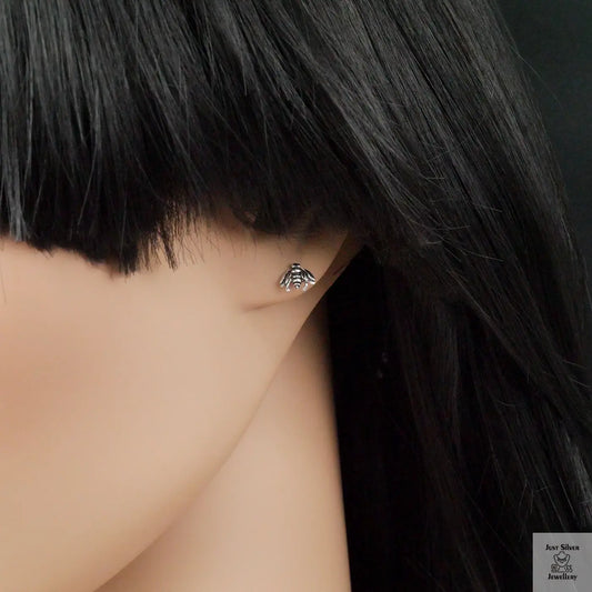 Close-up of an ear wearing a silver bee-shaped earring with dark hair.