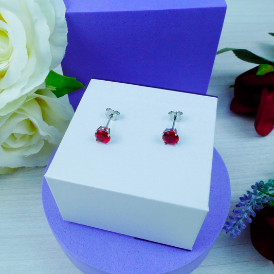 Red gemstone earrings on a white box with purple base and floral decorations.