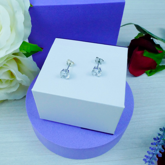 Silver earrings on a white box with flowers in the background