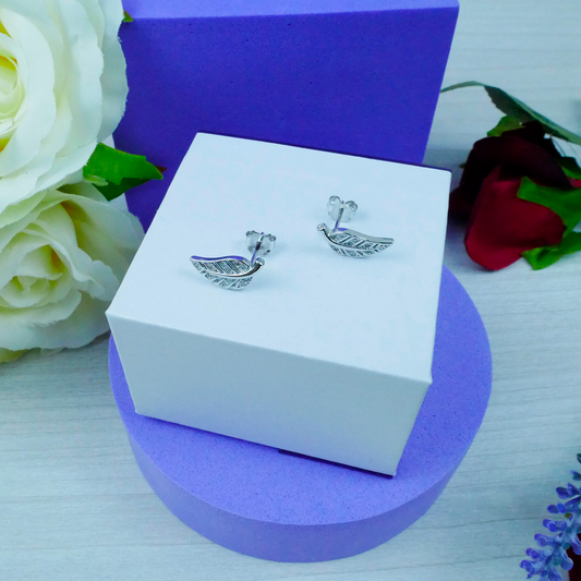 Silver boat-shaped earrings on a white box with purple base, surrounded by flowers.