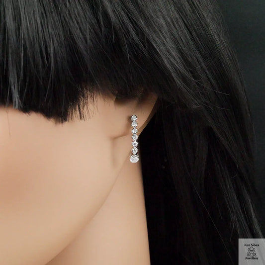 Close-up of a person wearing a dangling zirconia earring with a dark background