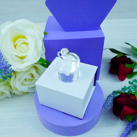 Ring in a clear box on a purple stand with flowers in the background