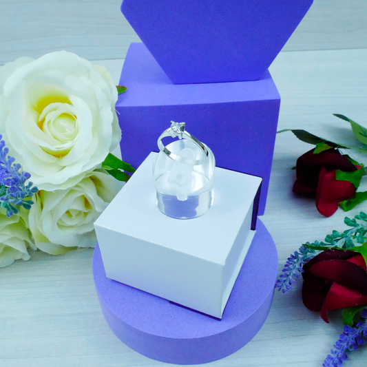 Ring on a stand with a purple and white box, surrounded by flowers on a light background