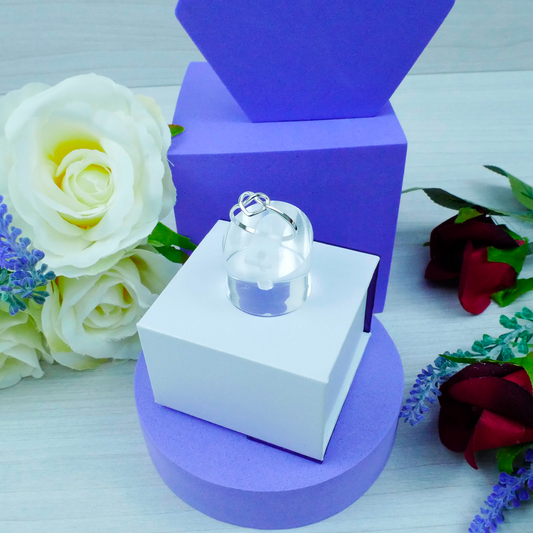 Clear glass pendant on a white stand with purple base, surrounded by flowers.