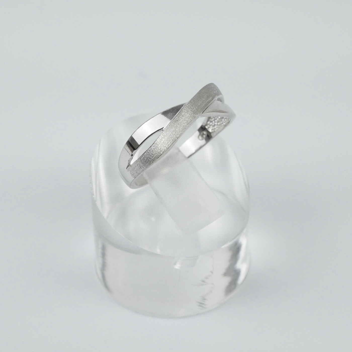 Silver two-tone ring on a clear crystal block against a light grey background
