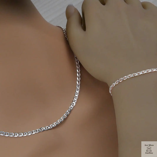 Silver marina chain necklace and bracelet on a person's wrist against a neutral background