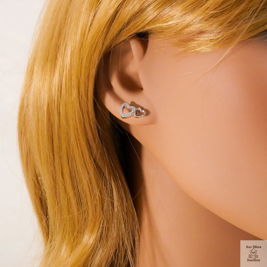 Close-up of an ear wearing a heart-shaped earring with blonde hair.