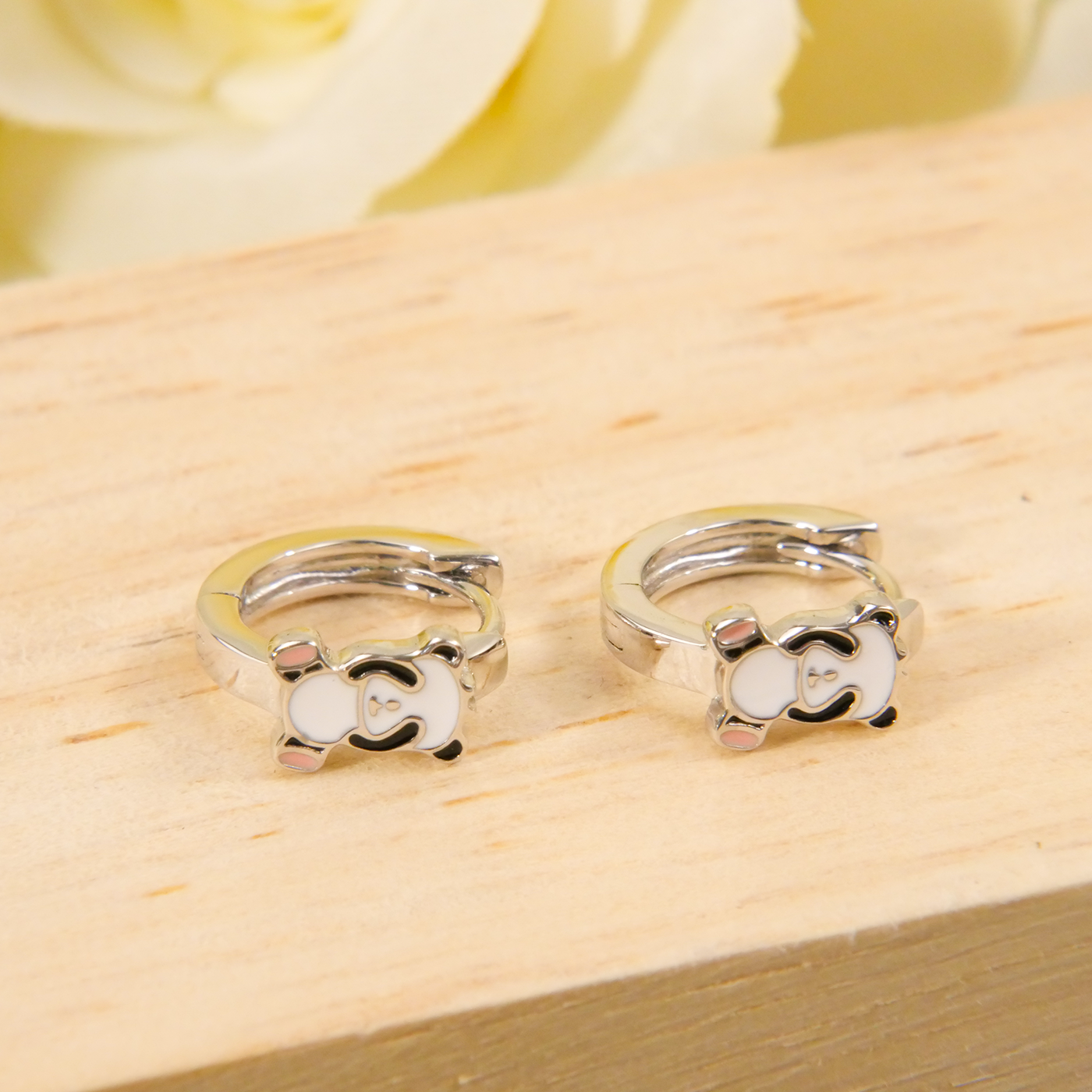 Pair of silver hoop earrings on a wooden surface with a blurred floral background