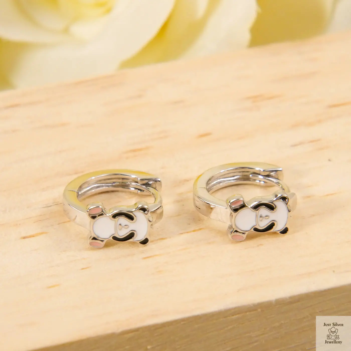 Pair of silver hoop earrings on a wooden surface with a blurred floral background