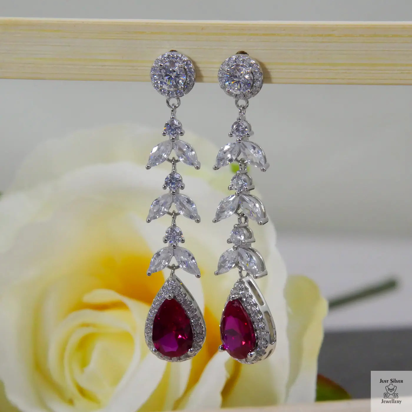 Silver earrings with red zircon gemstones on a wooden stand with a rose in the background
