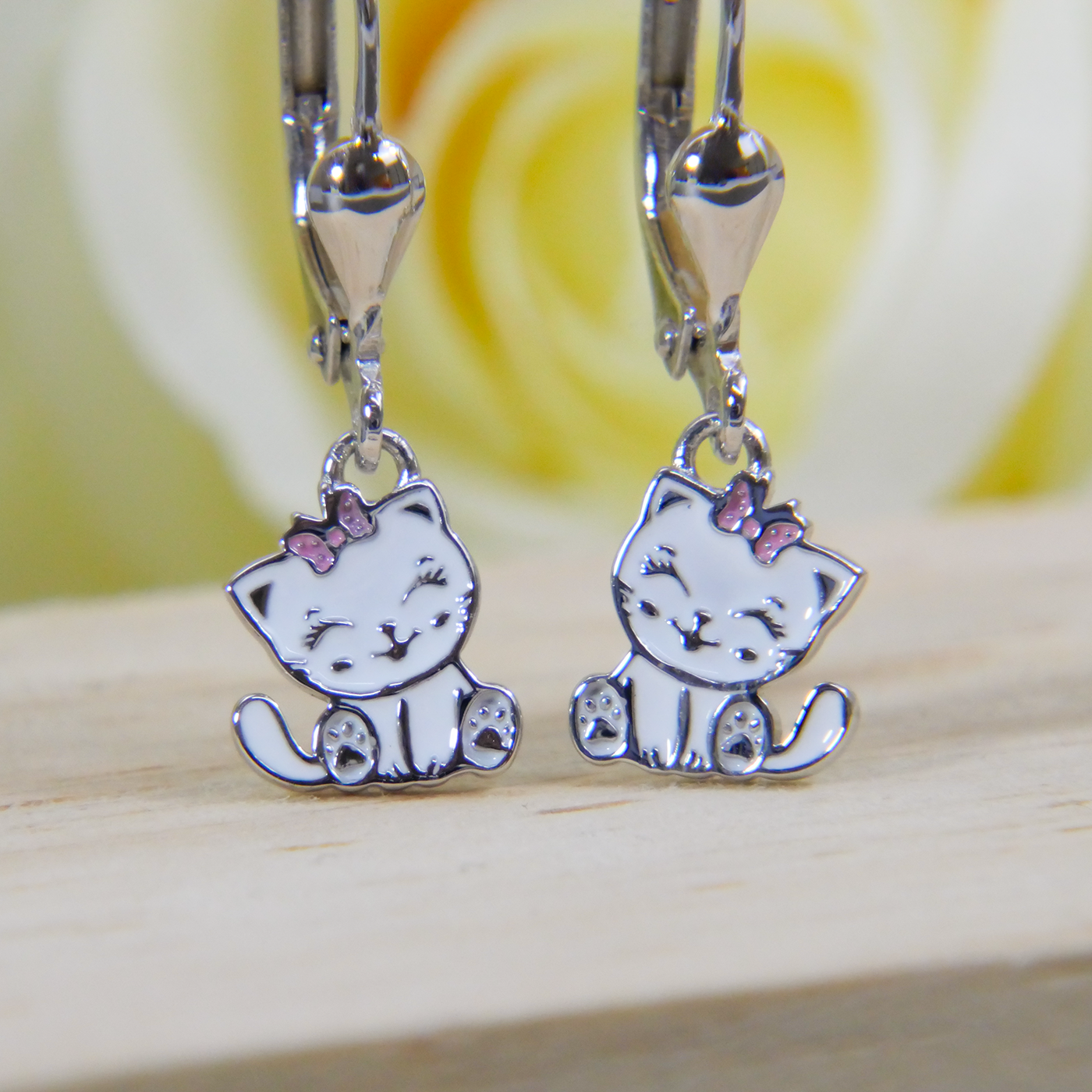 Silver cat-shaped earrings with pink bows on a wooden surface.