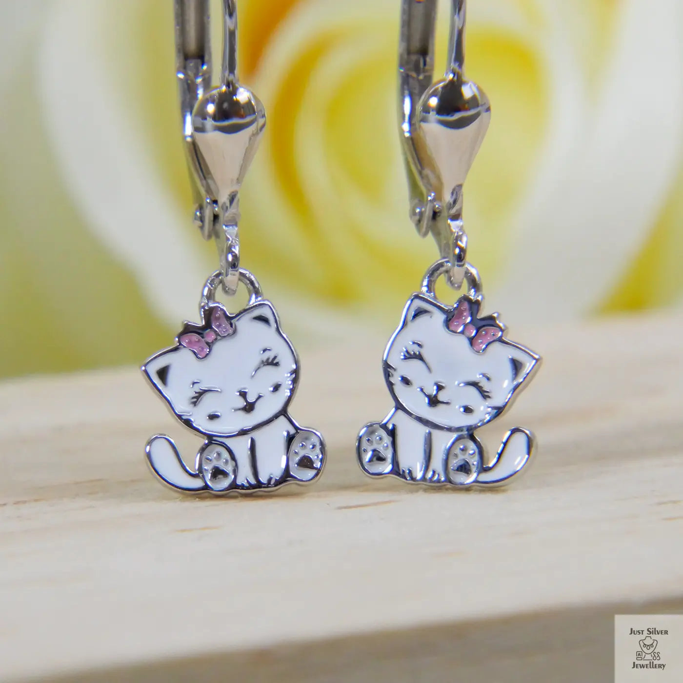 Silver cat-shaped earrings with pink bows on a wooden surface.