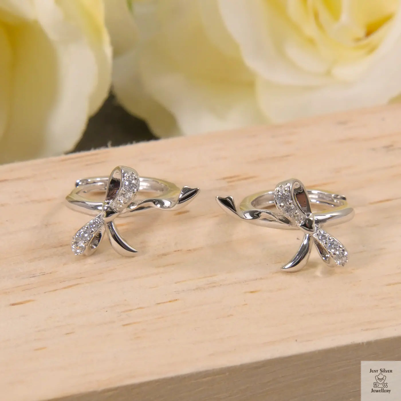 Two silver bow-shaped rings on a wooden surface with yellow roses in the background