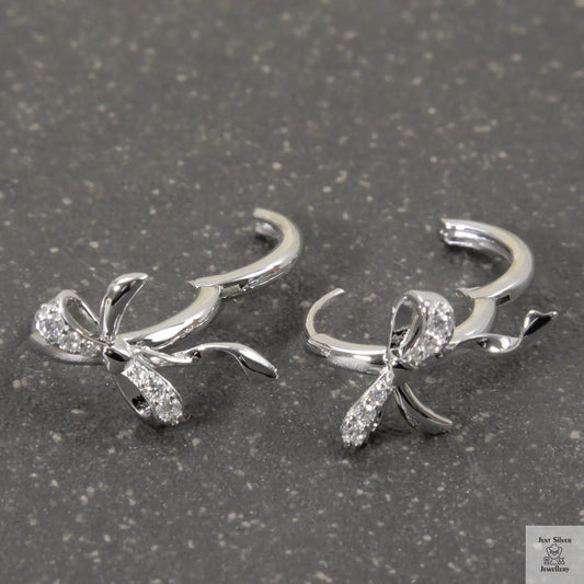 Silver bow-shaped earrings with clear stones on a gray surface
