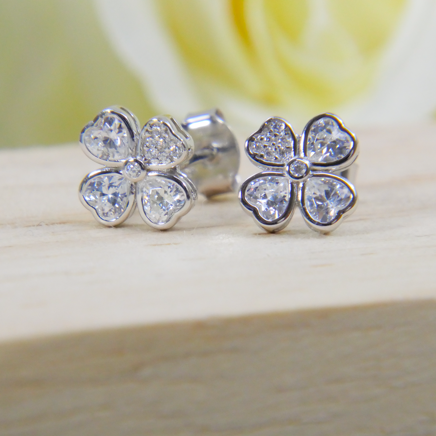 Silver four-leaf clover earrings with clear gemstones on a wooden surface.