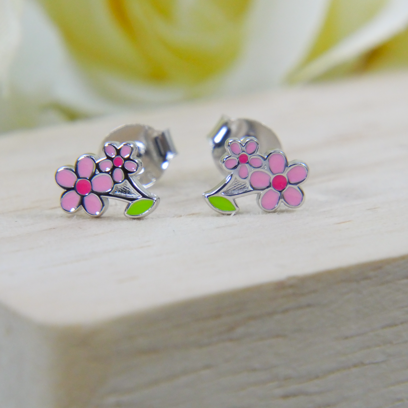 Silver earrings with pink floral designs on a wooden surface