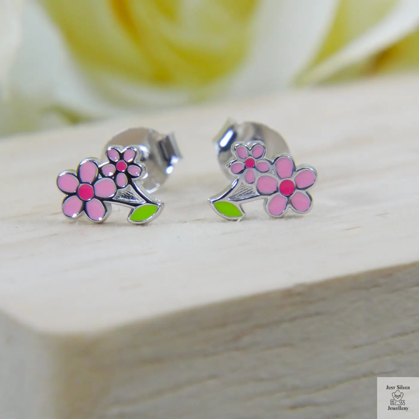 Silver earrings with pink floral designs on a wooden surface