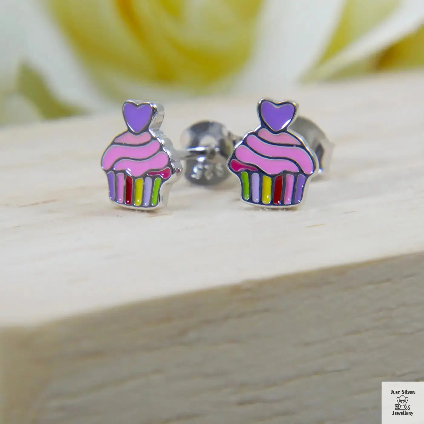 Cupcake-shaped earrings with colorful stripes on a wooden surface
