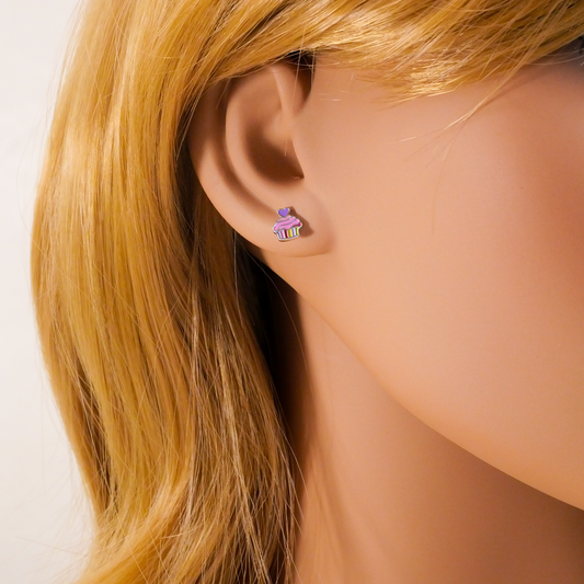 Close-up of an ear wearing a small earring with a cupcake design, against a neutral background.