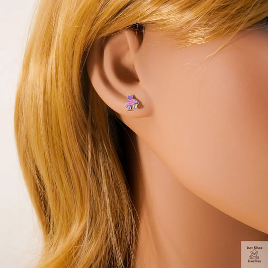 Close-up of an ear wearing a small earring with a cupcake design, against a neutral background.