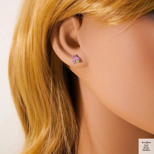 Close-up of an ear wearing a small earring with a cupcake design, against a neutral background.