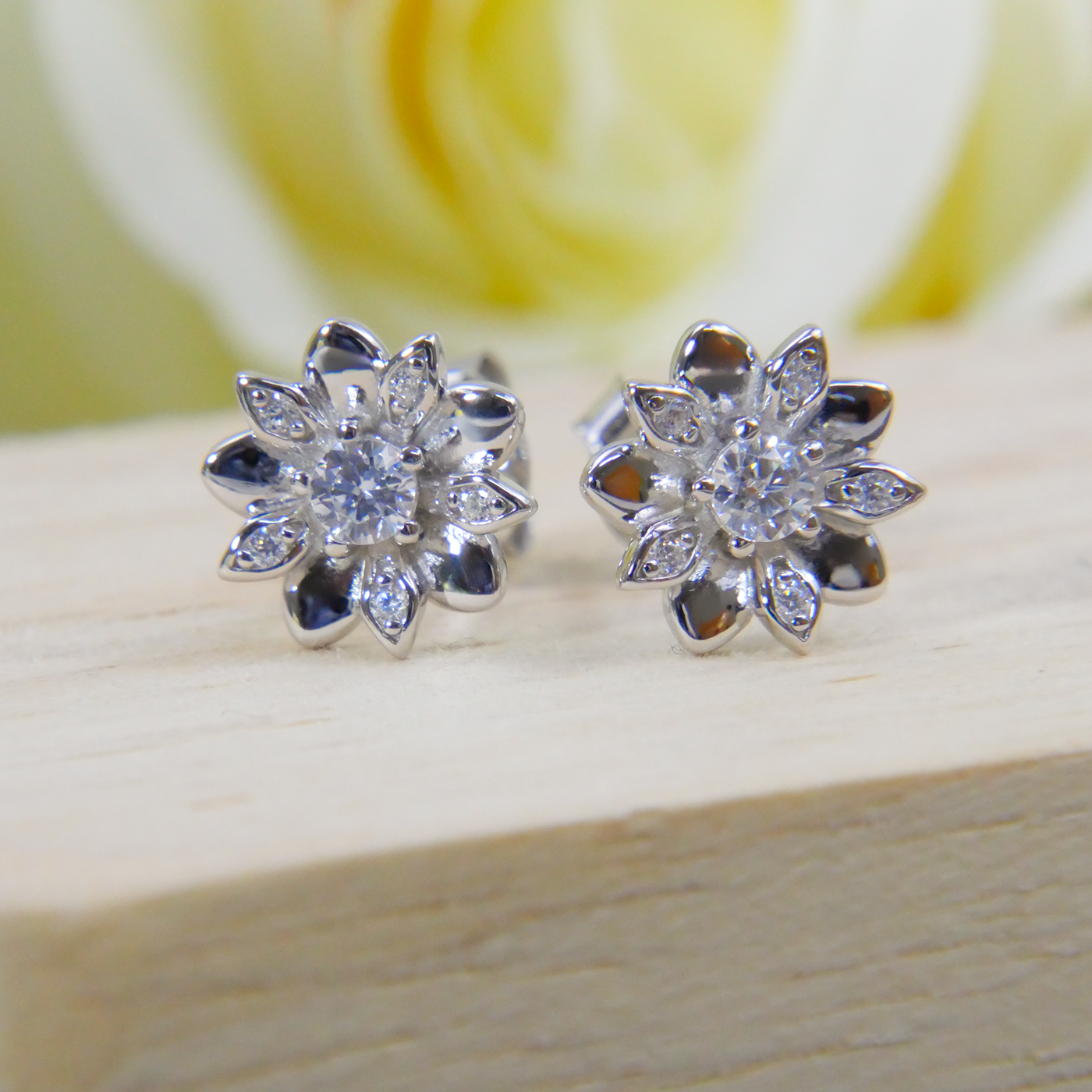 Silver flower-shaped earrings on a wooden surface with a blurred yellow rose in the background