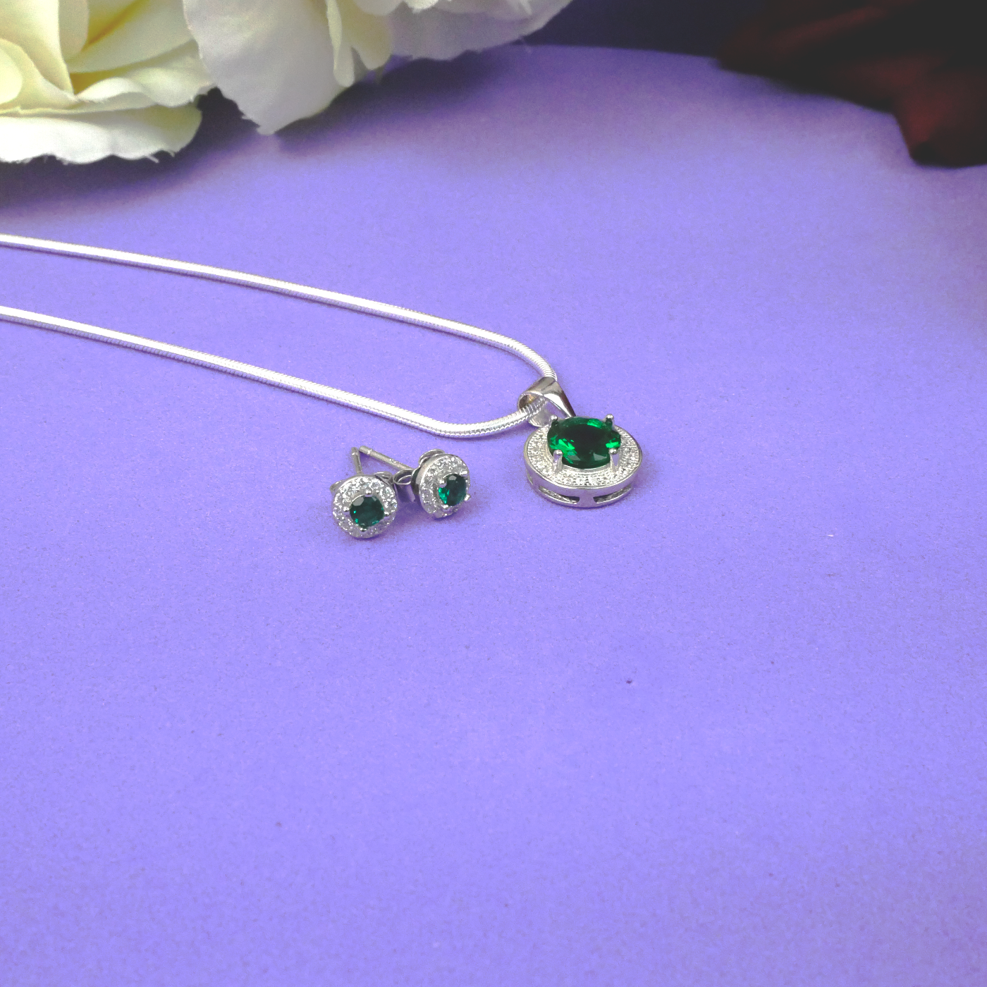 Silver jewelry set with green gemstones on a purple surface with white flowers.
