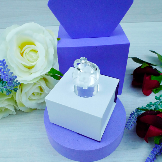 Silver ring in a white box on a purple stand with flowers in the background
